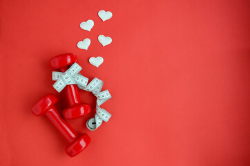 Two red dumbbells, white measuring tape, hearts on red background with copy space. Concept of Valentines day, healthy lifestyle, giving gifts, love of sports, shopping