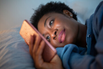 Close up African American woman looking at mobile phone while in bed
