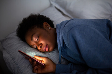 Close up African American woman holding mobile phone and sleeping