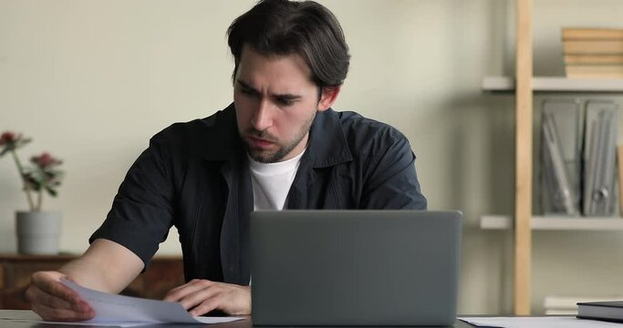 Perplexed millennial man office employee sit at desk do paperwork, learn written information frowning, faced with lack of ideas in problem solution, creative crisis, business challenge, issues concept
