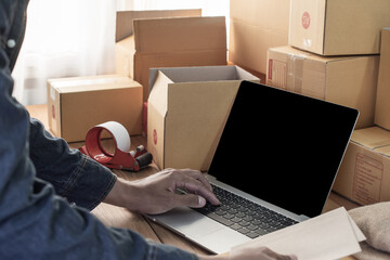 business owner working with laptop, packing the order for shipping to customer. male entrepreneur...