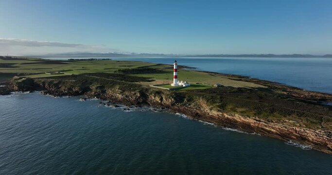 an aerial view of tarbat ness lighthouse on easter ross in the highlands of scotland near inverness showing blue sky and calm seas with the lighthouse dominating the scene and rocks