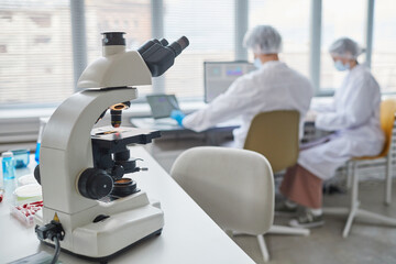 Close-up of microscope on the table in the laboratory with two scientists in the background