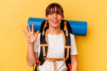 Young Argentinian hiker woman isolated on yellow background smiling cheerful showing number five with fingers.