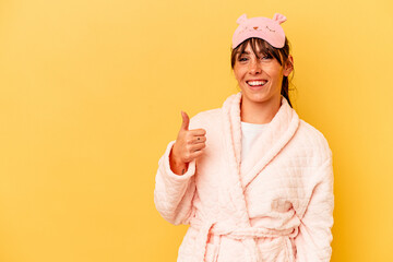 Young Argentinian woman wearing a pajama isolated on yellow background smiling and raising thumb up