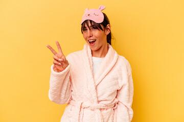 Young Argentinian woman wearing a pajama isolated on yellow background joyful and carefree showing a peace symbol with fingers.