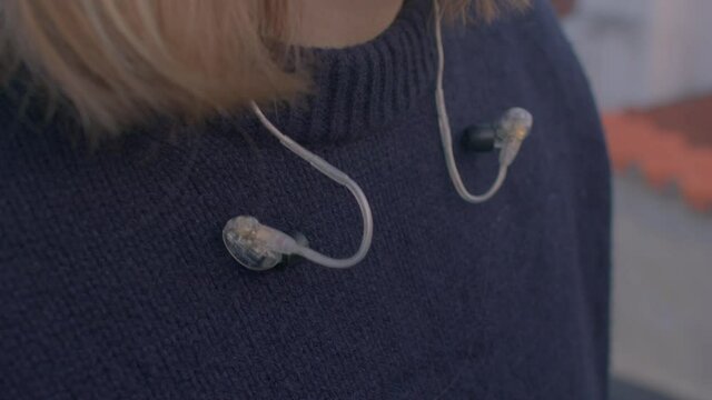 Speakers earplugs on woollen sweater. The ends of the hair are visible. A device to listen to sounds in mountainous places. The web of device usage.