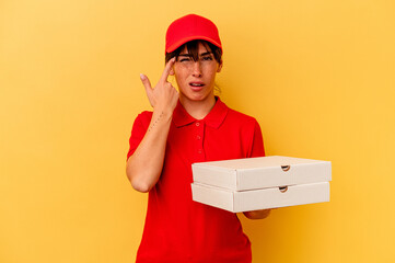 Young delivery woman holding pizzas isolated on yellow background showing a disappointment gesture with forefinger.