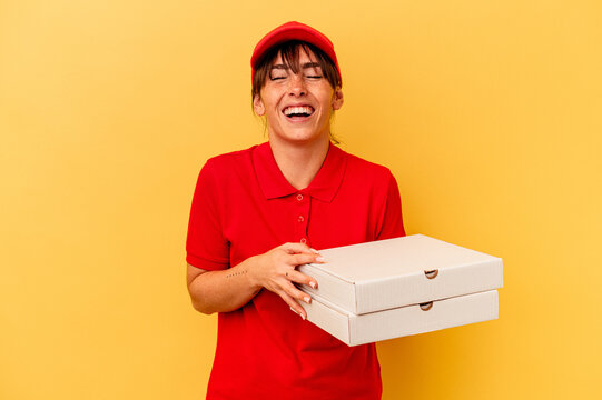 Young delivery woman holding pizzas isolated on yellow background laughing and having fun.