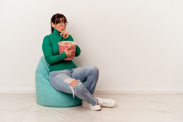 Young Argentinian woman eating popcorns on a puff isolated on white background keeping a secret or asking for silence.