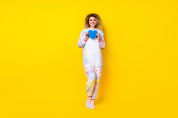 Full length body size view of attractive cheery girl in pajama holding blue form heart isolated on bright yellow color background