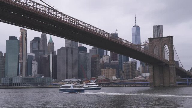 New York, USA, 2019. East river ferry is moving under Brooklyn bridge towards Downtown. One World Trade Center on background
