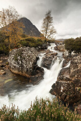 Fototapeta na wymiar Beautiful Waterfall At Buachaille Etive Mor In The Scottish Highlands with rainy clouds in background..