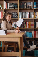 Attractive happy young girl student studying at the college library, sitting at the desk
