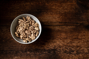Walnuts in a plate. Dark wooden background. Healthy, wholesome food. Place for your text.