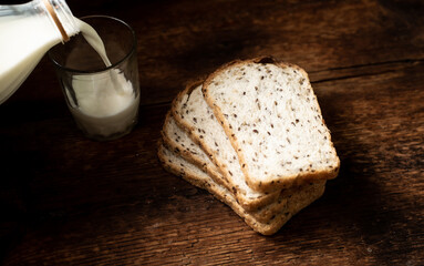Pieces of bread with seeds and milk are poured into a glass. Dark wooden background. Morning breakfast. Healthy food.