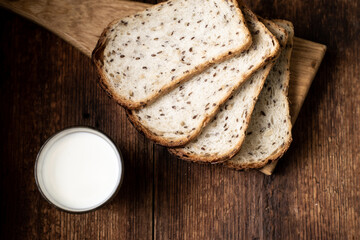 A full glass of milk. Bread in the background is blurred. Dark wooden background. Morning breakfast. Rustic style