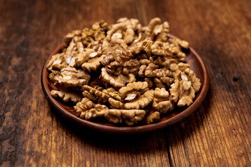 Fototapeta na wymiar Peeled walnuts on a plate. Dark wooden background. Vegetarian, healthy food.