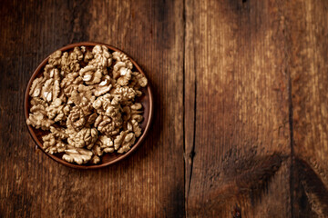 Peeled walnuts on a plate. Dark wooden background. Vegetarian, healthy food. View from above. Place for your text.