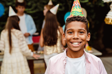 Black boy in party cone smiling at camera during birthday party
