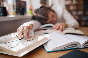 Young women got asleep on the books while studying holding reading glasses