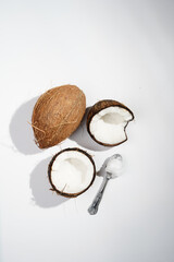 Cracked open coconut and a tea spoon with coconut oil on a white surface
