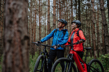 Fototapeta na wymiar Senior couple bikers with e-bikes admiring nature outdoors in forest in autumn day.