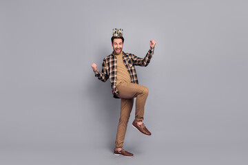Photo of rich lucky guy dressed checkered shirt glasses golden crown rising fists isolated grey color background