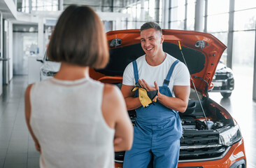 Owner standing near the man that repairing automobile indoors. Professional service