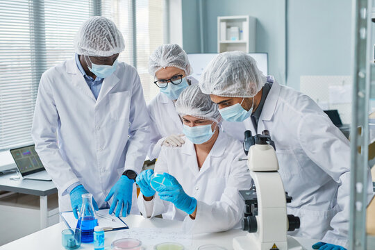 Group Of Scientists In Protective Masks Examining Samples In Tube In Team And Developing New Medicine From Virus In The Lab