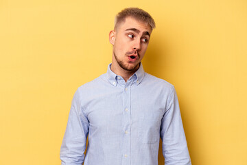 Young caucasian man isolated on yellow background looks aside smiling, cheerful and pleasant.