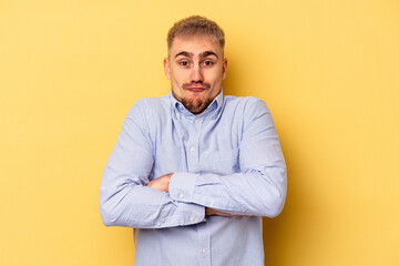 Young caucasian man isolated on yellow background shrugs shoulders and open eyes confused.