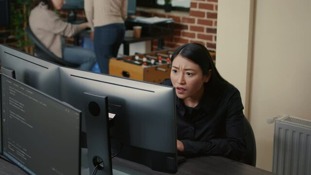 Portrait of asian programer focused on writing code encounters unexpected compiling error sitting at desk in software development office. Coder having system failure while creating algorithm.