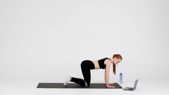 Sporty woman training with elastic band in front of laptop in studio