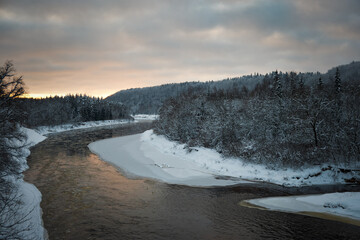 river in winter evening sunset dusk with snowy forest on shores