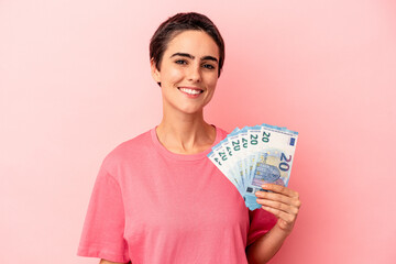 Young caucasian woman holding banknotes isolated on pink background happy, smiling and cheerful.