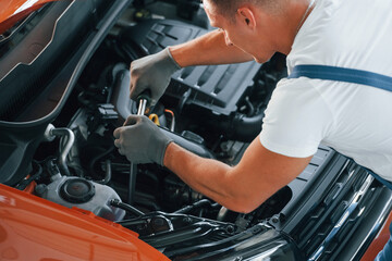 View from above. Man in uniform is repairing broken automobile indoors