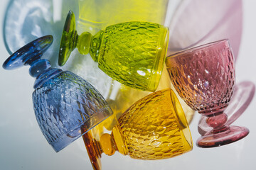 Stylish colored faceted glasses with shadows lay on a white table. Top view. Flat lay.