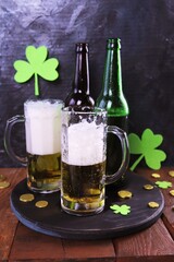 Patrick day, foamy beer in glass mugs and a bottle, gold coins on a wooden table, green shamrock on a dark background, party, congratulation, postcard