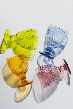 Four stylish colorful faceted glasses with shadows lay on a white table. Top view. Flat lay.