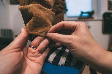 Hands placing a pin in the hem of a pair of pants 
