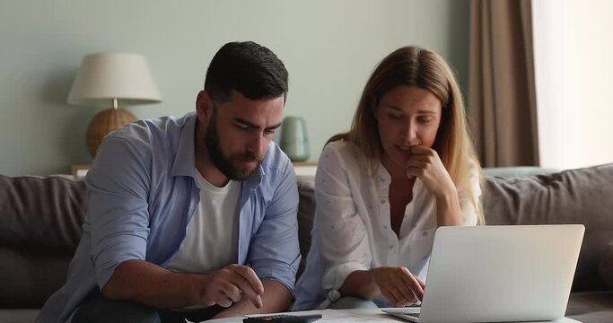 Unhappy young couple analyze financial documents at home stressed annoyed with too high utility charges. Worried spouses see budget deficit debt in bank report have difficulties with family business