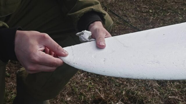 Man hands who repairs drone wing. Man glues a piece of foam plastic to wing.