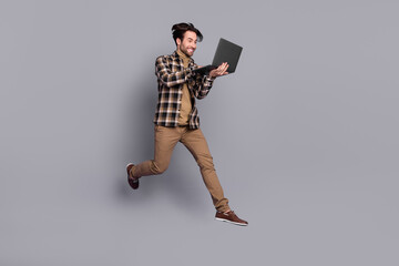 Photo of sweet cheerful man wear plaid shirt jumping high typing modern gadget isolated grey color background