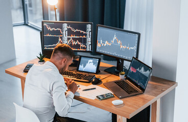Stock market. Young businessman in formal clothes is in office with multiple screens