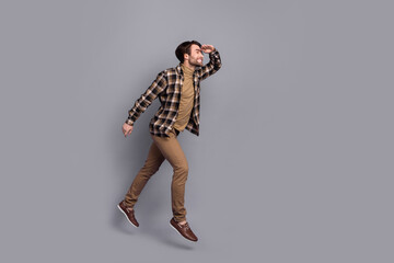 Photo of cheerful dreamy man wear plaid shirt jumping running far away empty space isolated grey color background