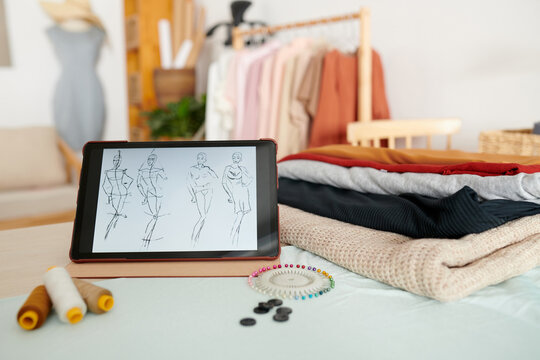 Tablet computer with fashion sketches nest to stack of various fabrics