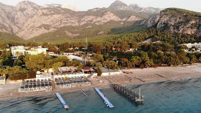 Aerial view of the rows of sun loungers on the sea beach and a large hotel with many pools on the shore of a mountain town