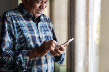Happy older man while using smartphone at home.