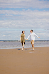 Fototapeta na wymiar a couple of a man and a woman are walking on the beach or running along the sand along the seashore. beautiful and young European man and woman on a romantic walk in nature, a couple in love, a happy